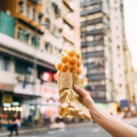 human hand holding freshly made traditional street snack egg waffle against city street in hong kong - junk food stock pictures, royalty-free photos & images