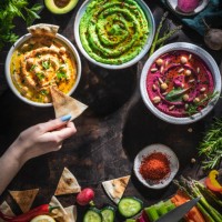 hummus bowls of chickpeas, avocado and beetroot female hand dip with cut vegetables for dipping - food stock pictures, royalty-free photos & images