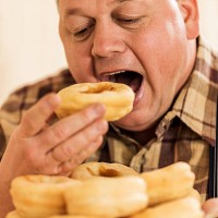 hungry overweight man eating donuts. - junk food stock pictures, royalty-free photos & images