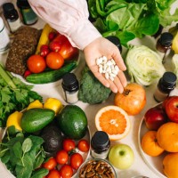 in the dietitian's office, the table is set with vegetables, fruits, nuts, bread, herbs, capsules of drugs in the palm - food stock pictures, royalty-free photos & images