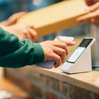 in the restaurant, a woman uses her smartphone to make a payment with the cashier. she scans the qr code using a card reader to complete a convenient contactless payment. at the same time, the cashier hands over the purchased