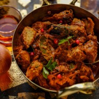 indian chicken vindaloo in a brass wok ready to be served, on a grunge metal, wood and gold leaf background with fresh vegetables, spices and red wine vinegar, ingredients of the dish, accompanying the scene. - food stock pic
