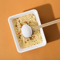instant noodles with fresh egg in a white plastic plate, on an orange background - junk food stock pictures, royalty-free photos & images