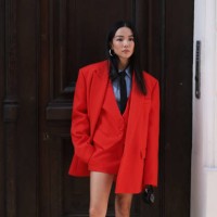 Is seen wearing a blue shirt with a black tie, a black Valentino bag, silver earrings, a red skirt, an oversized red blazer as well as a red vest...