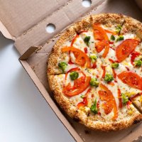 italian pizza in a pizza box and for delivery, on a white background or table. pizza margarita with tomatoes and cheese and broccoli, without meat. the concept of vegetarian food, fast junk food. delivery to your home or work