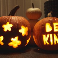 jack-o-lantern pumpkins illuminated outside a house at night, one with flower cutouts and the other with the words be kind, halloween decorations - garden decoration stockfoto's en -beelden