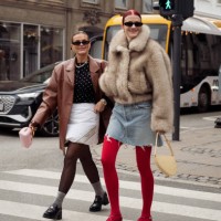 Janka Polliani wears black loafers, grey socks, a white Prada pillow skirt, a black top, and a brown leather jacket and Marianne Theodorsen wears red...