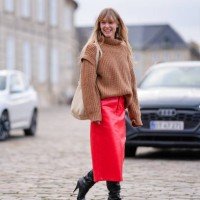 Jeanette Madsen wears a brown oversized ribbed wool pullover, a white leather bag, a red leather midi skirt, knee high high heels pointed leather...