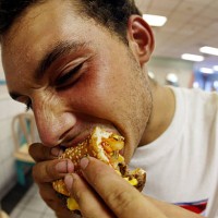 Jeff Baughman bites into his double cheeseburger with a Super Fries and a Super Coke on July 18, 2002 at a McDonalds in Miami Beach, Florida. The...