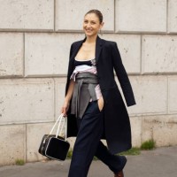 Jenny Walton wears a black and white Miu Miu leather bag, a black long coat, a grey Miu Miu sweater around the waist, a black and white Miu Miu tank...