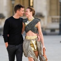 Jonathan Nielssen wears a black wool pullover, dark gray suit pants, Renate Reinsve wears a gray with black leopard embossed pattern and gold fringed...