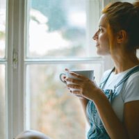 jonge mooie vrouw is op zoek door het raam en het drinken van koffie in de ochtend - coffee stockfoto's en -beelden