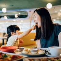 joyful young asian mother and lovely little daughter enjoying lunch together in restaurant. they are sharing food, enjoying family bonding time and a happy meal at the dining table. family and eating out lifestyle - food stoc