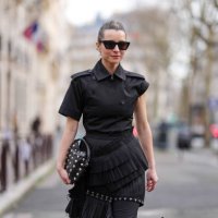 Julia Comil wears black sunglasses, a black top / jacket with ruffle details, a black leather bag with studs, outside Rokh, during the Womenswear...