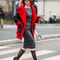 Julia Hobbs Dag wears black sunglasses, dark gray fitted midi dress, black bright cherry red aviator coat, black sheer mesh Prada compression socks,...