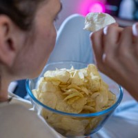 June 2023, Saxony, Leipzig: ILLUSTRATION - A woman is eating chips in a living room in front of the TV. Photo: Hendrik Schmidt/dpa