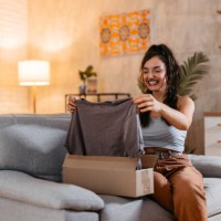 junge frau packt ein paket mit einem neuen hemd aus - fashion stock-fotos und bilder