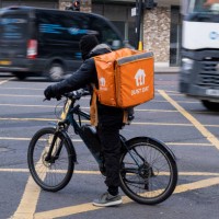 Just Eat takeaway delivery cycle courier waits at a road junction as fast moving heavy traffic passes on 3rd December 2024 in London, United Kingdom....