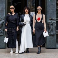Justyna Czerniak wears black net skirt, black asymmetric top, white shoes, tights, Paco Rabanne bag & Xiayan Guo wears white dress, black blazer &...