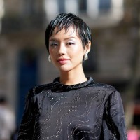 Khanh Linh wears earrings, a black lustrous silk mini dress with long sleeves and printed geometric patterns, outside Stella McCartney, during the...