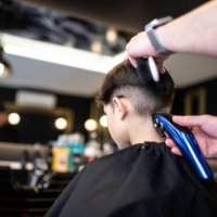kleiner 7-jähriger junge geht in einen friseursalon, um einen modernen haarschnitt zu bekommen, rückansicht rasieren - hairstyle stock-fotos und bilder
