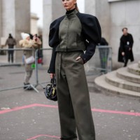Kristina Romanova wears a khaki and black jacket, khaki wide-leg pants, a black leather bag with gold details, outside Sacai, during the Menswear...