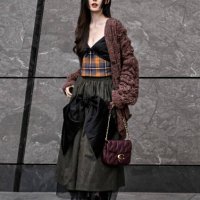 Lực Na Trát is seen wearing a brown cardigan, plaid top, brown and black ruffled skirt, black Coach boots and Coach bagoutside the Coach 1941 show...