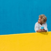 latin woman holding cell phone leaning on yellow wall over blue background. technology and social media concept. banner template, copy space for text on the side. - fashion fotografías e imágenes de stock