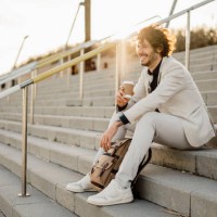 laughing businessman with coffee to go and backpack sitting on stairs outdoors - junk food stock pictures, royalty-free photos & images