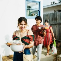 laughing friends walking into backyard with trays of food for barbecue on summer evening - food photos et images de collection