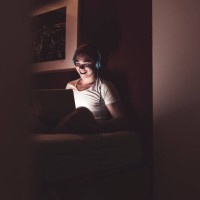 laughing man with headphones and laptop sitting on couch at home - fashion stock-fotos und bilder