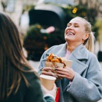 laughing women hold christmas presents and street food enjoying christmas market with friend - junk food stock pictures, royalty-free photos & images