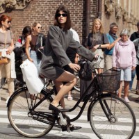 Lea Naumann riding a bicycle wears grey long sleeve mini dress and black shoes outside the Gestuz show during day four of the Copenhagen Fashion Week...