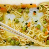 leftovers of eaten instant noodles sprinkled with spices, vegetables, herbs and freeze-dried meat. there are wooden chopsticks nearby. asian chicken soup with ramen noodles on the dining kitchen table. the end of the meal. si