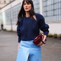 Leia Sfez wears a dark blue ribbed knitted wool pullover with puff sleeves, a burgundy leather bag, a pastel pale slit skirt in leather , pointed...