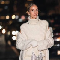 Leonie Hanne wears a black and large rhinestones pendant earrings, a white wool turtleneck sleeveless oversized pullover, a white fluffy long coat, a...