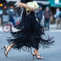 Leonie Hanne wears a neon yellow quilted leather puff bag, a black midi skirt with fringes, black high heels sandals / shoes, outside Proenza...