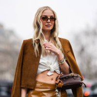 Leonie Hanne wears dark brown sunglasses, white collar tied Miu Miu shirt, dark brown unzipped Miu Miu suede jacket, gold Cartier Bracciale Juste...