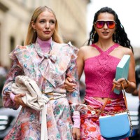 Leonie Hanne wears earrings, a pink turtleneck, a long sleeves, ruffled, light pink dress with colorful flowers print and a lavaliere, a white belt...