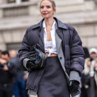 Leonie Hanne wears white Miu Miu bralette, white buttoned up long sleeve tied shirt, dark gray Miu Miu blazer jacket, black high waisted Miu Miu over...