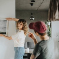 lesbian woman taking advice from girlfriend while hanging frame on wall at home - home decoration stock pictures, royalty-free photos & images