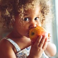 linda niña de raza mixta comiendo una manzana roja fresca, comiendo saludable en casa - food fotografías e imágenes de stock