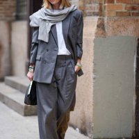 Lisa Aiken wears a light gray scarf, a dark gray oversized blazer jacket, a white t-shirt, matching suit pants, a black leather bag, outside Proenza...