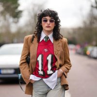 Loic Hornecker wears transparent frames black lens sunglasses, white buttoned up long sleeve shirt, dark green pattern necktie, dark red San...