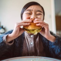 lovely cheerful girl enjoying her homemade burger at home - junk food stock pictures, royalty-free photos & images