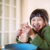 lovely cheerful girl smiling joyfully at the camera while enjoying snack with her sister in front of a food stall in the street - junk food stock pictures, royalty-free photos & images