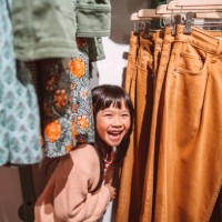 lovely little girl smiling joyfully behind a clothes rack while shopping in a clothing store - fashion stock pictures, royalty-free photos & images