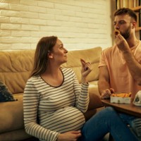 lovely man and his pregnant woman eating onion rings at home - junk food stock pictures, royalty-free photos & images