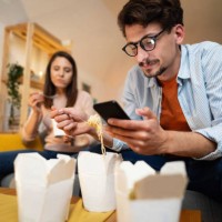 low-angle view of a young man using a phone while eating - junk food stock pictures, royalty-free photos & images