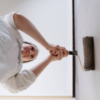low angle of woman catching with two hands a roller of grey painting on a brown wall. - home decoration stock pictures, royalty-free photos & images